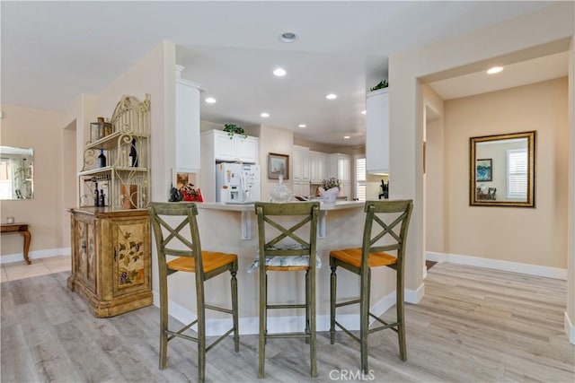 2747 Traditions Loop, Paso Robles, CA 93446 - kitchen with white refrigerator with ice dispenser, a breakfast bar area, light wood-type flooring, white cabinetry, and recessed lighting