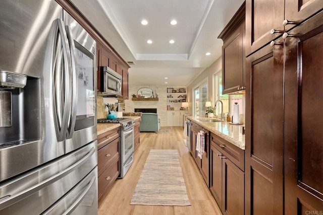 5431 Stirrup Way, Oceanside, CA 92057 - kitchen featuring appliances with stainless steel finishes, light wood-style flooring, a fireplace, light stone countertops, and a raised ceiling