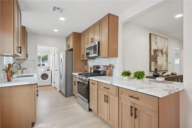 8115 Etiwanda Ave, Reseda, CA 91335 - kitchen featuring appliances with stainless steel finishes, washer / dryer, a sink, light stone counters, and light wood finished floors