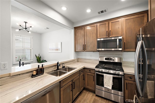 9 Reese Crk, Ladera Ranch, CA 92694 - kitchen with stainless steel appliances, a sink, light stone counters, light wood-style floors, and a chandelier