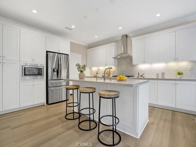 159 Frazier, Irvine, CA 92620 - kitchen featuring appliances with stainless steel finishes, wall chimney exhaust hood, a breakfast bar, white cabinets, and light wood-style floors
