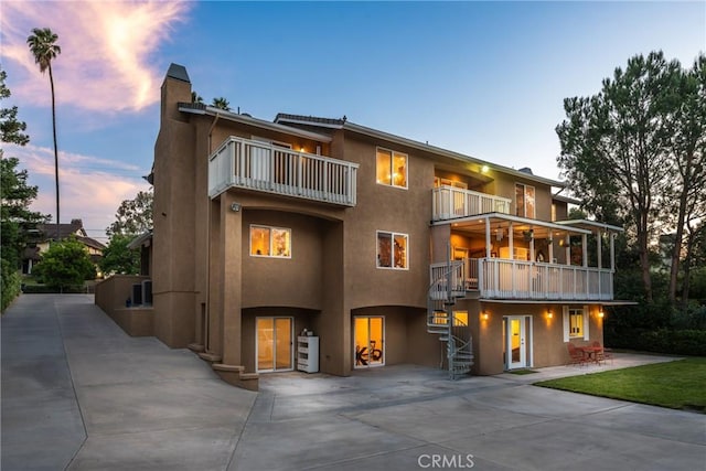 1377 Knoll Rd, Redlands, CA 92373 - back of house at dusk with a balcony, stairs, a patio area, stucco siding, and a chimney