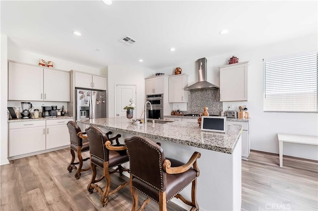 29485 Whitewood St, Menifee, CA 92584 - kitchen featuring wall chimney range hood, appliances with stainless steel finishes, a kitchen breakfast bar, light wood-style floors, and tasteful backsplash
