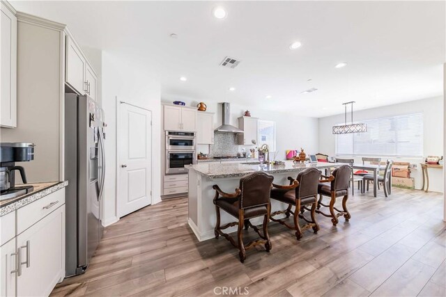 29485 Whitewood St, Menifee, CA 92584 - kitchen featuring appliances with stainless steel finishes, wall chimney exhaust hood, light wood-style floors, a kitchen breakfast bar, and a kitchen island with sink