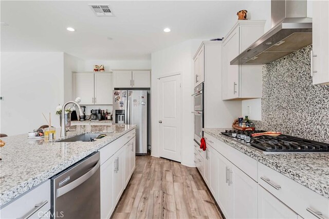 29485 Whitewood St, Menifee, CA 92584 - kitchen featuring appliances with stainless steel finishes, wall chimney exhaust hood, white cabinetry, light wood-style flooring, and backsplash