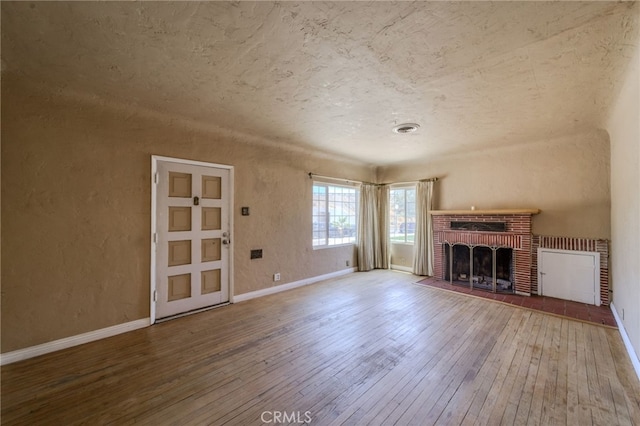 503 California Ave, Needles, CA 92363 - unfurnished living room with wood-type flooring, a brick fireplace, baseboards, and a textured wall