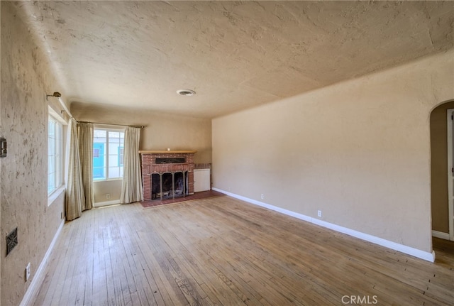 503 California Ave, Needles, CA 92363 - unfurnished living room featuring a fireplace, hardwood / wood-style flooring, arched walkways, baseboards, and a textured ceiling