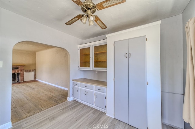 503 California Ave, Needles, CA 92363 - unfurnished dining area featuring arched walkways, ceiling fan, light wood-style floors, baseboards, and a brick fireplace