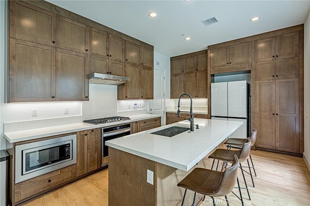 20754 W Bur Oak Cir, Porter Ranch, CA 91326 - kitchen featuring stainless steel appliances, under cabinet range hood, light wood-type flooring, a kitchen bar, and a kitchen island with sink
