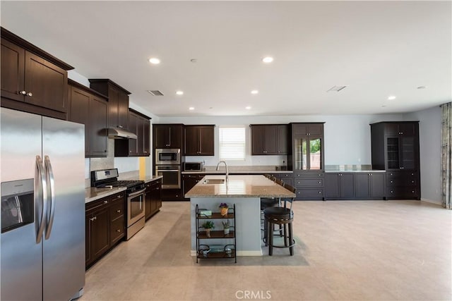 34901 Limecrest Pl, Murrieta, CA 92563 - kitchen with appliances with stainless steel finishes, under cabinet range hood, recessed lighting, a kitchen island with sink, and dark brown cabinetry