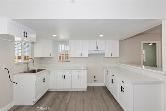 35010 Cedar Rd, Barstow, CA 92311 - kitchen with a sink, under cabinet range hood, light wood-type flooring, baseboards, and white cabinetry