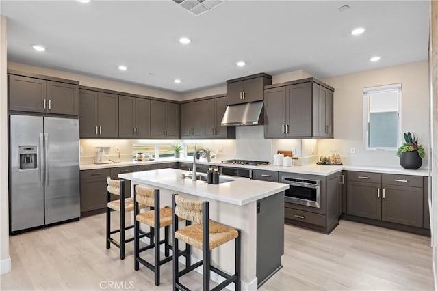 225 Waypoint, Tustin, CA 92782 - kitchen featuring appliances with stainless steel finishes, under cabinet range hood, light countertops, a center island with sink, and a kitchen bar
