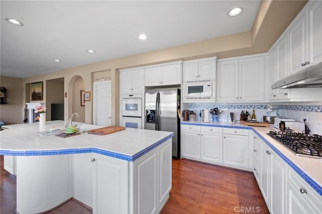 3262 Bluebird Cir, Simi Valley, CA 93063 - kitchen with white appliances, arched walkways, under cabinet range hood, white cabinetry, and recessed lighting
