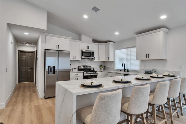16409 Barbee St, Fontana, CA 92336 - kitchen with stainless steel appliances, a peninsula, white cabinetry, a breakfast bar, and light wood-style floors