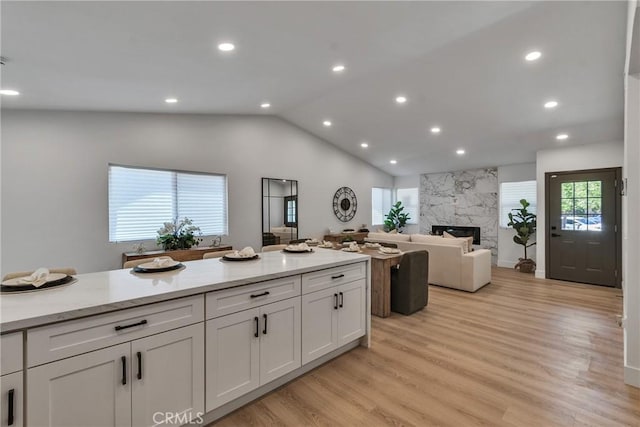 16409 Barbee St, Fontana, CA 92336 - kitchen with open floor plan, vaulted ceiling, white cabinetry, a high end fireplace, and light wood-type flooring