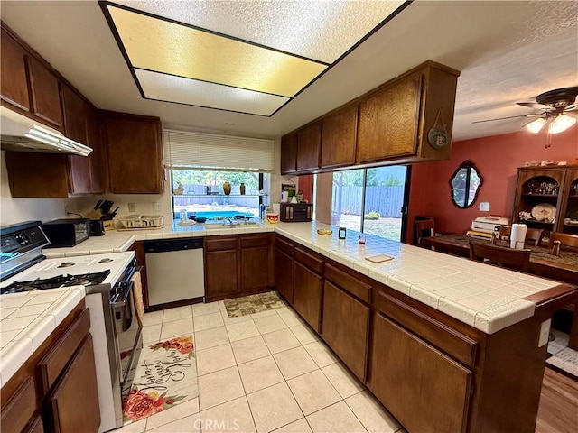 24859 Rock Springs Trl, Moreno Valley, CA 92557 - kitchen featuring range with gas stovetop, dishwasher, tile countertops, under cabinet range hood, and a peninsula