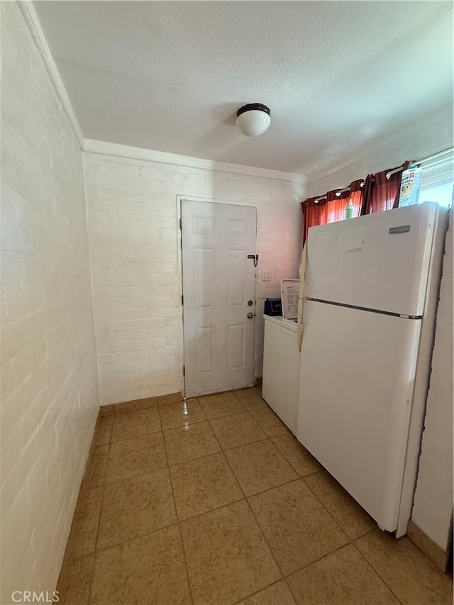 6733 Tamarisk Ave Unit 29, Palms, CA 92277 - kitchen featuring freestanding refrigerator, light tile patterned floors, washer / clothes dryer, brick wall, and a textured ceiling