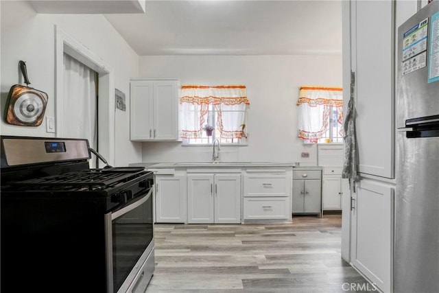 1732 W 48th St, Los Angeles, CA 90062 - kitchen featuring appliances with stainless steel finishes, a sink, light wood finished floors, white cabinets, and light countertops