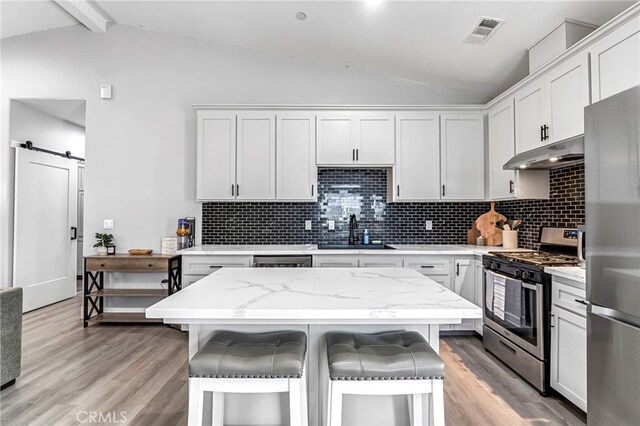 22375 Fairmead Cir, Chowchilla, CA 93610 - kitchen with appliances with stainless steel finishes, under cabinet range hood, a kitchen bar, light wood-style floors, and decorative backsplash