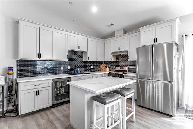 22375 Fairmead Cir, Chowchilla, CA 93610 - kitchen featuring appliances with stainless steel finishes, wine cooler, under cabinet range hood, light wood-style flooring, and vaulted ceiling
