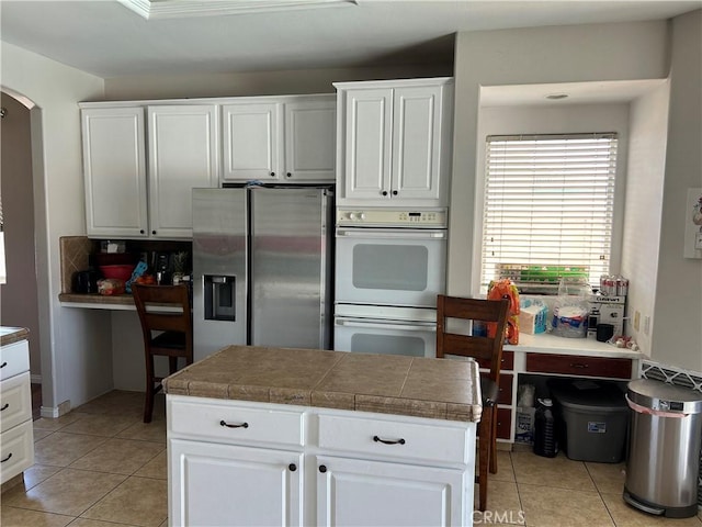5825 Sky Lakes Ave, Bakersfield, CA 93313 - kitchen with stainless steel refrigerator with ice dispenser, double oven, arched walkways, light tile patterned flooring, and white cabinetry