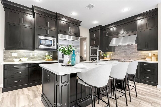 11 Goldenrod, Lake Forest, CA 92630 - kitchen with range hood, built in appliances, tasteful backsplash, a kitchen breakfast bar, and a kitchen island with sink