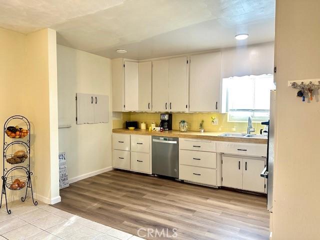 27441 Villa Ave, Highland, CA 92346 - kitchen featuring stainless steel dishwasher, a sink, light countertops, white cabinetry, and light wood-style flooring