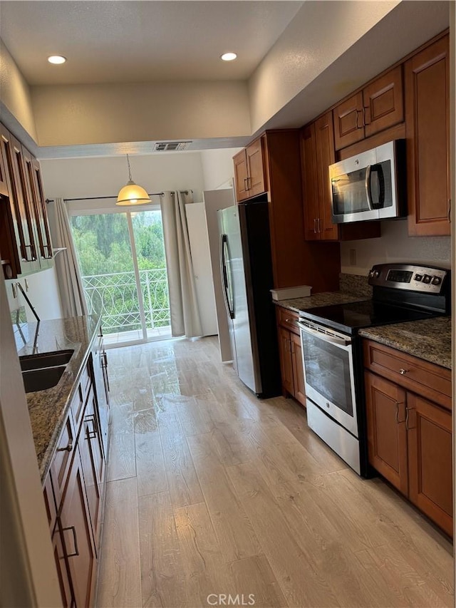 19029 Nordhoff St Unit 309, Northridge, CA 91324 - kitchen with appliances with stainless steel finishes, light wood finished floors, dark stone counters, brown cabinetry, and pendant lighting