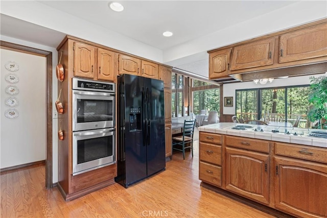 524 Golf Course Rd, Lake Arrowhead, CA 92352 - kitchen featuring black refrigerator with ice dispenser, double oven, light wood-style floors, tile counters, and brown cabinetry