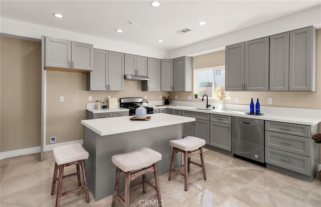 565 N Meridian Ave, San Bernardino, CA 92410 - kitchen with stainless steel dishwasher, gas stove, gray cabinetry, under cabinet range hood, and a kitchen bar