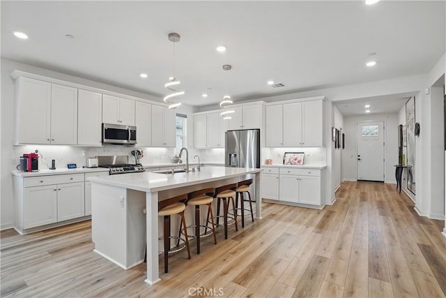 28410 Orange Park Dr, Castaic, CA 91384 - kitchen featuring stainless steel appliances, an island with sink, white cabinetry, light countertops, and a kitchen bar