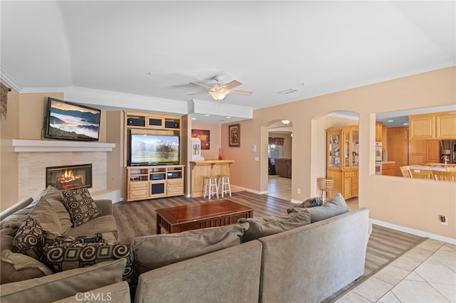 1042 Coronet Dr, Riverside, CA 92506 - living room featuring arched walkways, a ceiling fan, crown molding, a fireplace, and light tile patterned floors