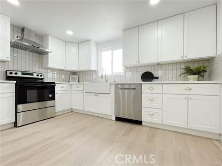 109 S San Antonio Ave, Upland, CA 91786 - kitchen featuring appliances with stainless steel finishes, wall chimney range hood, light countertops, white cabinets, and light wood finished floors