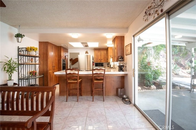 5295 Bronson Way, Riverside, CA 92506 - kitchen featuring freestanding refrigerator, brown cabinets, a peninsula, a skylight, and light countertops