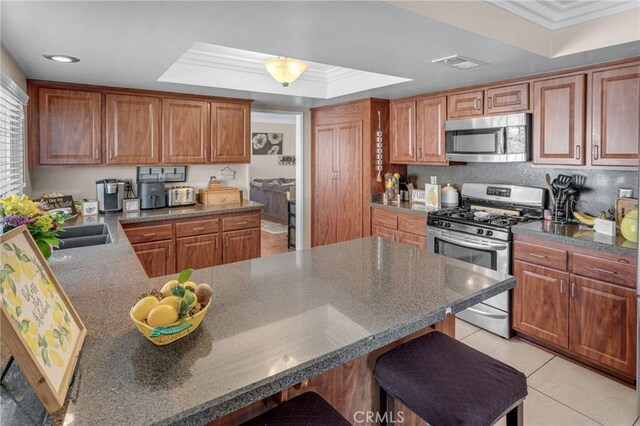 13520 Preciado Ave, Chino, CA 91710 - kitchen with stainless steel appliances, a raised ceiling, ornamental molding, a kitchen bar, and brown cabinetry