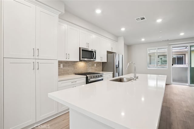 1549 Stratus Dr, Pomona, CA 91768 - kitchen with stainless steel appliances, an island with sink, white cabinetry, light wood finished floors, and recessed lighting
