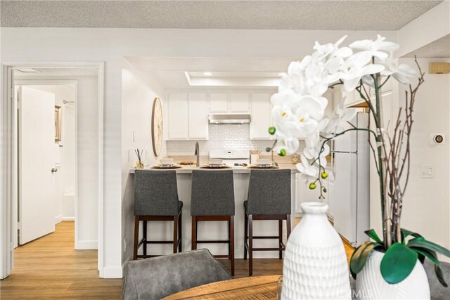 38 Woodleaf, Irvine, CA 92614 - kitchen with extractor fan, light wood finished floors, a kitchen breakfast bar, white cabinets, and decorative backsplash