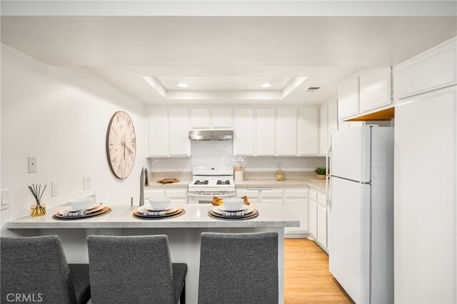 38 Woodleaf, Irvine, CA 92614 - kitchen with white appliances, under cabinet range hood, a peninsula, a tray ceiling, and light countertops