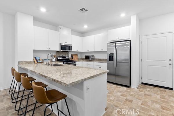 15940 Lasselle St Unit 1, Moreno Valley, CA 92551 - kitchen with stainless steel appliances, a kitchen breakfast bar, a peninsula, white cabinets, and recessed lighting