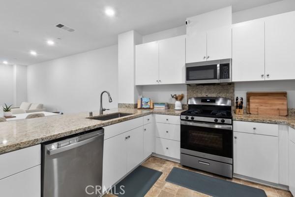 15940 Lasselle St Unit 1, Moreno Valley, CA 92551 - kitchen featuring appliances with stainless steel finishes, white cabinets, light stone countertops, a peninsula, and recessed lighting