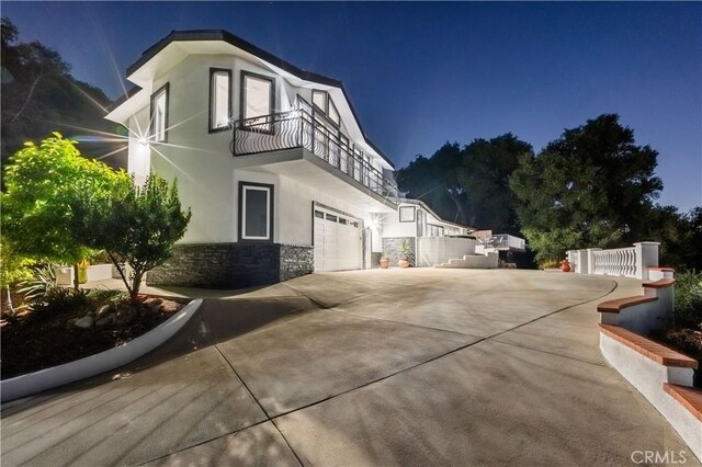 14757 Rockhill Dr, Hacienda Heights, CA 91745 - property exterior at twilight with a balcony, stone siding, stucco siding, an attached garage, and driveway