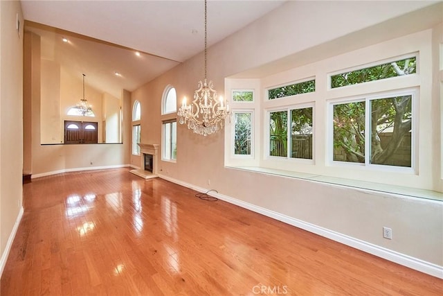 26821 Moore Oaks Rd, Laguna Hills, CA 92653 - unfurnished living room featuring a chandelier, healthy amount of natural light, high vaulted ceiling, a glass covered fireplace, and wood finished floors