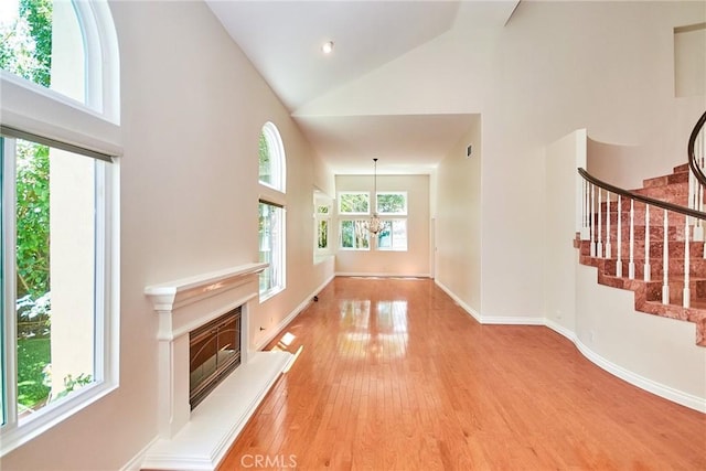 26821 Moore Oaks Rd, Laguna Hills, CA 92653 - unfurnished living room featuring high vaulted ceiling, stairs, light wood-type flooring, a glass covered fireplace, and a chandelier