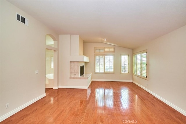 26821 Moore Oaks Rd, Laguna Hills, CA 92653 - unfurnished living room with light wood-style flooring, vaulted ceiling, a tiled fireplace, and arched walkways