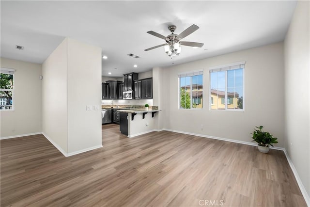 8022 Cresta Bella Rd, Rancho Cucamonga, CA 91730 - kitchen featuring a breakfast bar area, dark cabinets, stainless steel appliances, open floor plan, and light wood-style floors