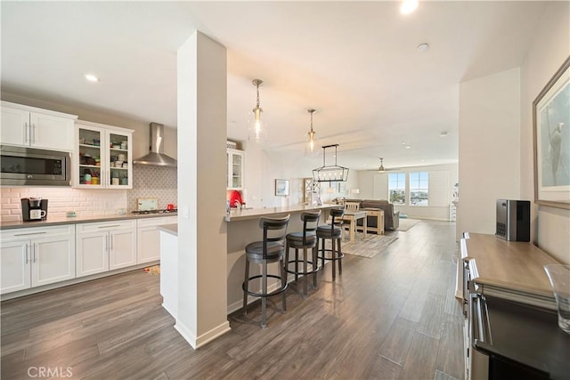4048 Tradewinds Dr, Oxnard, CA 93035 - kitchen featuring stainless steel microwave, wall chimney range hood, a breakfast bar, white cabinets, and recessed lighting