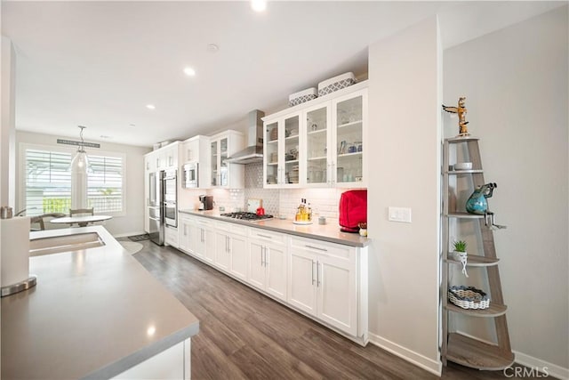 4048 Tradewinds Dr, Oxnard, CA 93035 - kitchen featuring wall chimney range hood, appliances with stainless steel finishes, decorative backsplash, white cabinets, and dark wood-style flooring