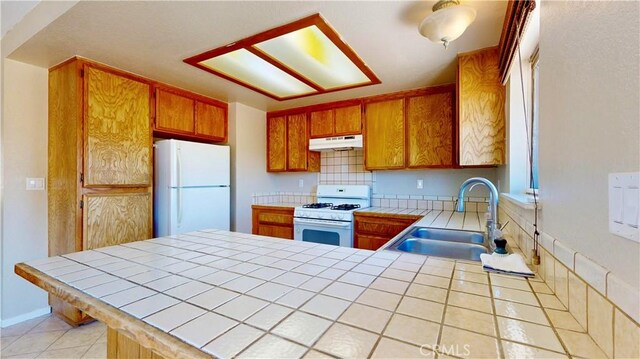 19171 Carlisle Rd, Apple Valley, CA 92307 - kitchen featuring white appliances, tile counters, under cabinet range hood, and brown cabinets