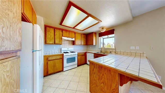 19171 Carlisle Rd, Apple Valley, CA 92307 - kitchen featuring white appliances, under cabinet range hood, tile counters, a peninsula, and brown cabinets