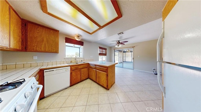19171 Carlisle Rd, Apple Valley, CA 92307 - kitchen featuring white appliances, a peninsula, brown cabinets, tile counters, and light tile patterned flooring